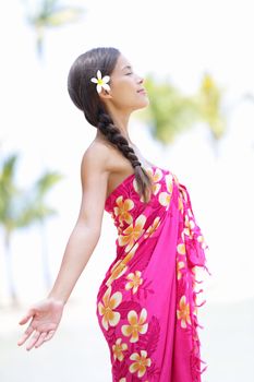 Beach woman on Hawaii relaxing enjoying the sun in serene relaxed pose. Hawaiian scene with beautiful mixed race Asian and Caucasian female model wearing sarong.