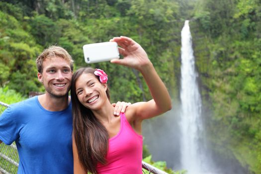 Couple tourists taking self portrait with camera phone on Hawaii, Big Islands, Akaka Falls. Happy cheerful young multicultural couple on travel.