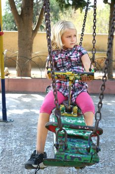 A beautiful blond girl looks sad on a rusty old swing