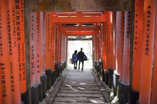 Two figures walking away from camera through lines of torii gates at the Fushimi Inari shrine in Kyoto, Japan