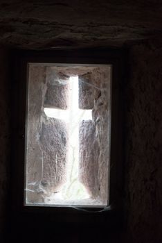 Contrasting light shines in the shape of a cross through the window of an old castle
