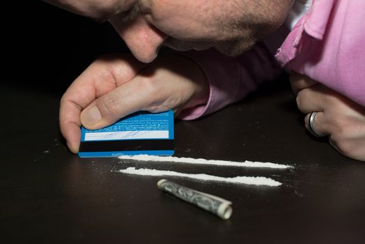 Drug abuse: Young man preparing cocaine for sniffing using a credit card.