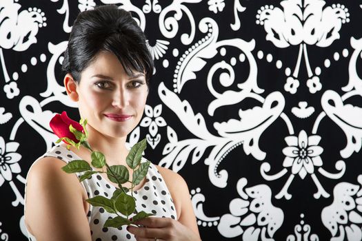 young woman in front of a black and white textured background with 60's inspired style holding a rose