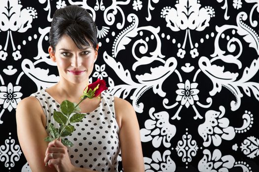 young woman in front of a black and white textured background with 60's inspired style holding a rose