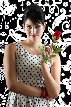 young woman in front of a black and white textured background with 60's inspired style holding a rose