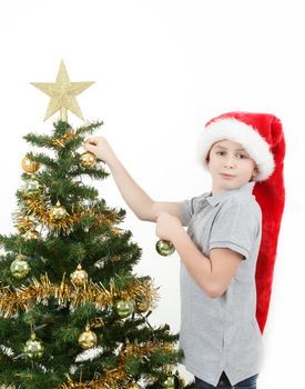 Boy with santa hat decorates the Christmas tree on white background