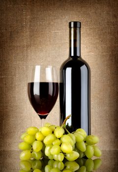 Bottle of red wine and grapes on a background canvas