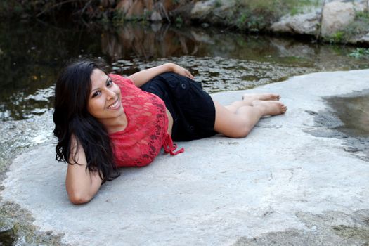 Hispanic woman lying at water edge of a creek.