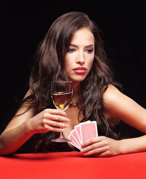 pretty young woman holding gambling cards and glass of wine on red table