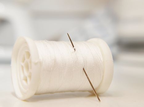 White thread on spool, laying down, with a needle