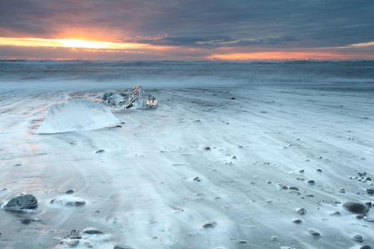 Ice on vocanic black sand iceland beach at sunset