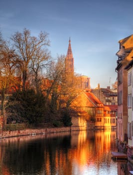 Colorful reflections of traditional houses in a small canal in Strasbourg. In the distance can be seen The Strasbourg Cathedral of Our Ladies.