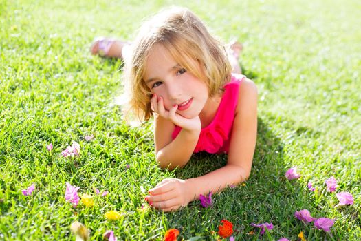 blond kid girl lying relaxed in garden grass with flowers smiling