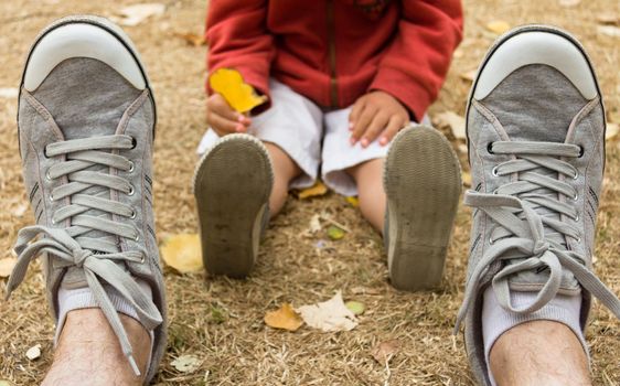 Sneakers front view of man sitting on field and back view of child´s snakers soles with a tree leaf in hand