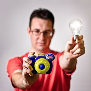 Photographer holding toy camera and handmade light bulb flash on gray background