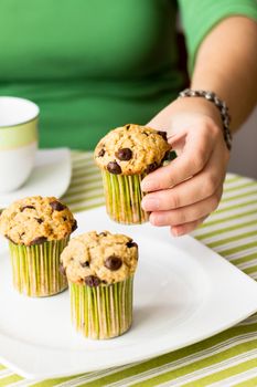 Nice girl hand taking delicious chocolate chip muffin at breakfast in green striped tablecloth