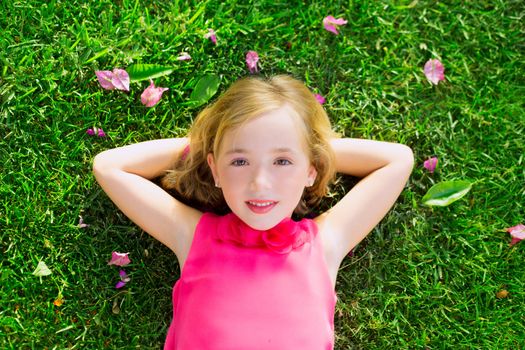 Blond kid girl lying on garden grass smiling happy aerial view