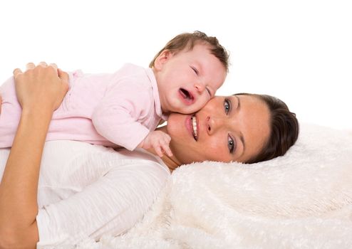 Baby girl crying and mother lying together on white fur blanket