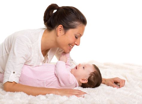 Baby girl and mother lying happy playing together on white fur blanket