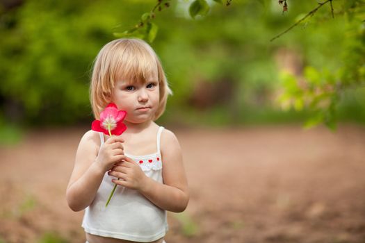 small serious girl with tulip outdoors in sunny day