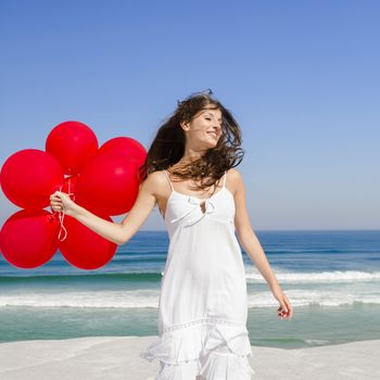 Beautiful girl with red ballons in the beach and wind blowing in the face