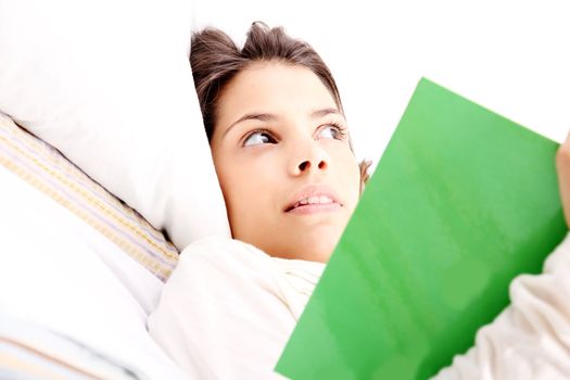 A young latin woman reading a book in bed.