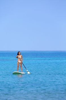 Hawaii beach lifestyle woman paddleboarding in bikini. Beautiful multiethnic woman sufing on stand up paddleboard on Big Island, Hawaii.