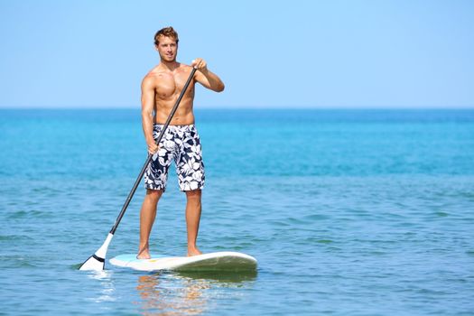 Stand up paddle board man paddleboarding on Hawaii standing happy on paddleboard on blue water. Young caucasian male model on Hawaiian beach on summer holidays vacation travel.