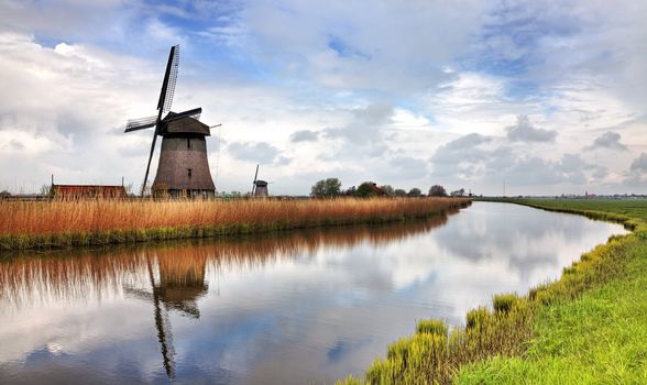 Image of a traditional Dutch windmill near a canal in a cloudy day.