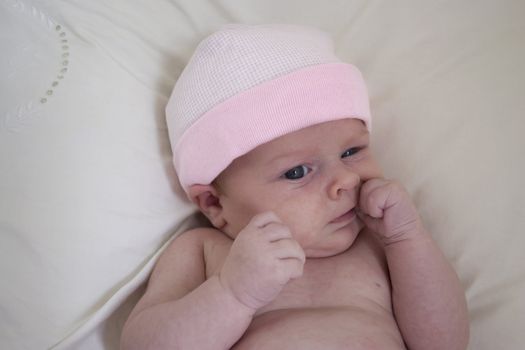 A newborn baby girl with a pink hat, sucking her thumb