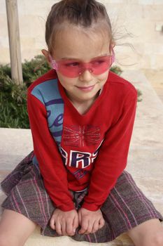 A young girl wearing pink sunglasses, smiling and not looking into the camera