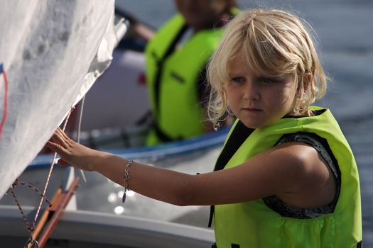 A young 8 year old girl is sailing in an optimist with a life jacket on