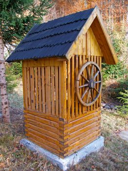 A lonely, wooden draw-well in the garden, with forest in the background