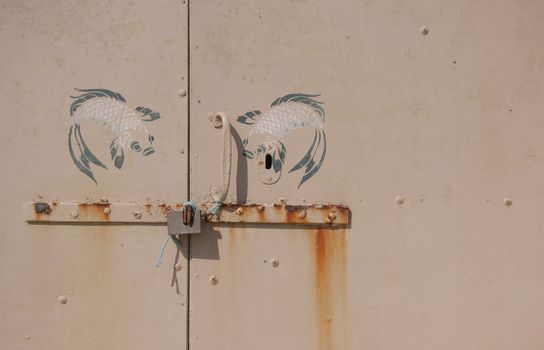 A rusty door with an old padlock, with two koi fish painted on top of lock. Copy space