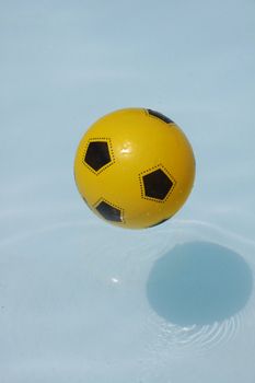 A yellow and black ball is floating in blue water