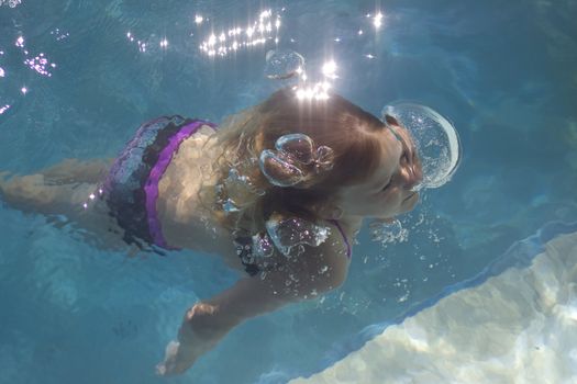 A young girl is resurfacing in a swimmingpool from a dive, while blowing bubbles