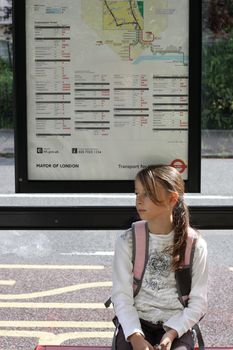Girl sitting at a busstop with a schoolbag