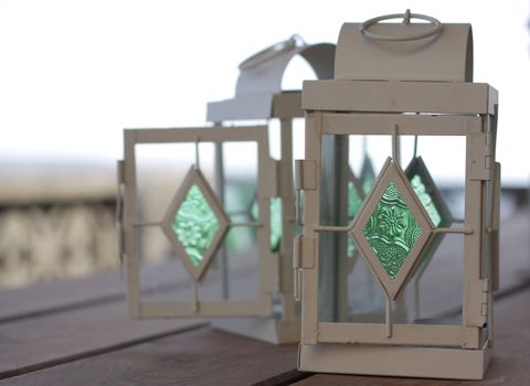 Two metal lanterns standing on a wooden table outdoors. With green coloured glass inserts.