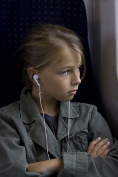 A young girl with headset sitting on a train, looking out of the window. 