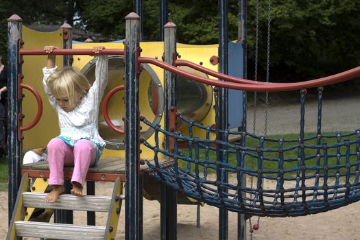 A little girl sitting on a climbing frame in a park