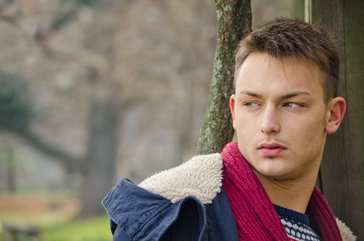 Attractive young male model outdoors in nature leaning on wood