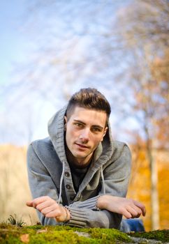 Handsome young man outdoors in nature lying on moss covered stone