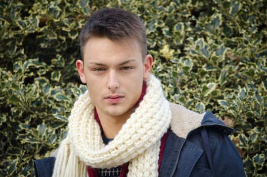 Attractive young man in winter clothes with holly bush behind