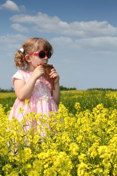 little girl standing in yellow flower field and play pan pipe