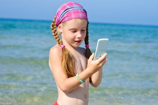 A little girl talks to mobile phone on the beach
