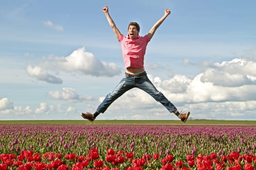 Young enthousiastic guy jumping up from the tulip fields in the Netherlands