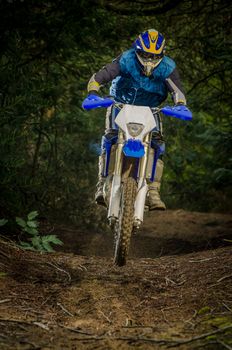 Enduro bike rider on action. Small jamp on muddy terrain.