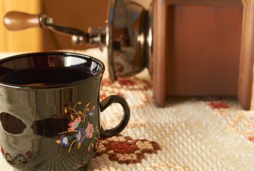 Manual coffee grinder and ceramic cup on woven tablecloth