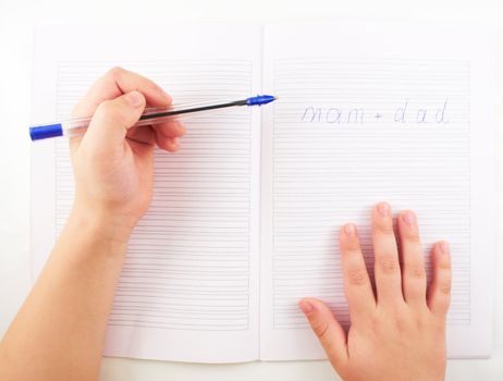 A small child's hand writing in notebook words with a ballpoint pen