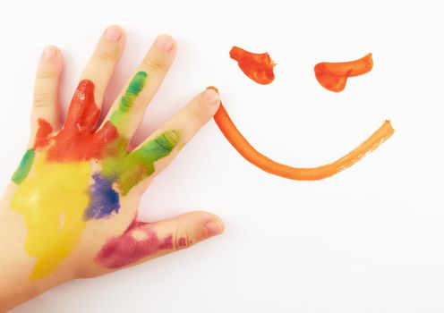 Child's hand stained in paint on white paper draws  a smiley face